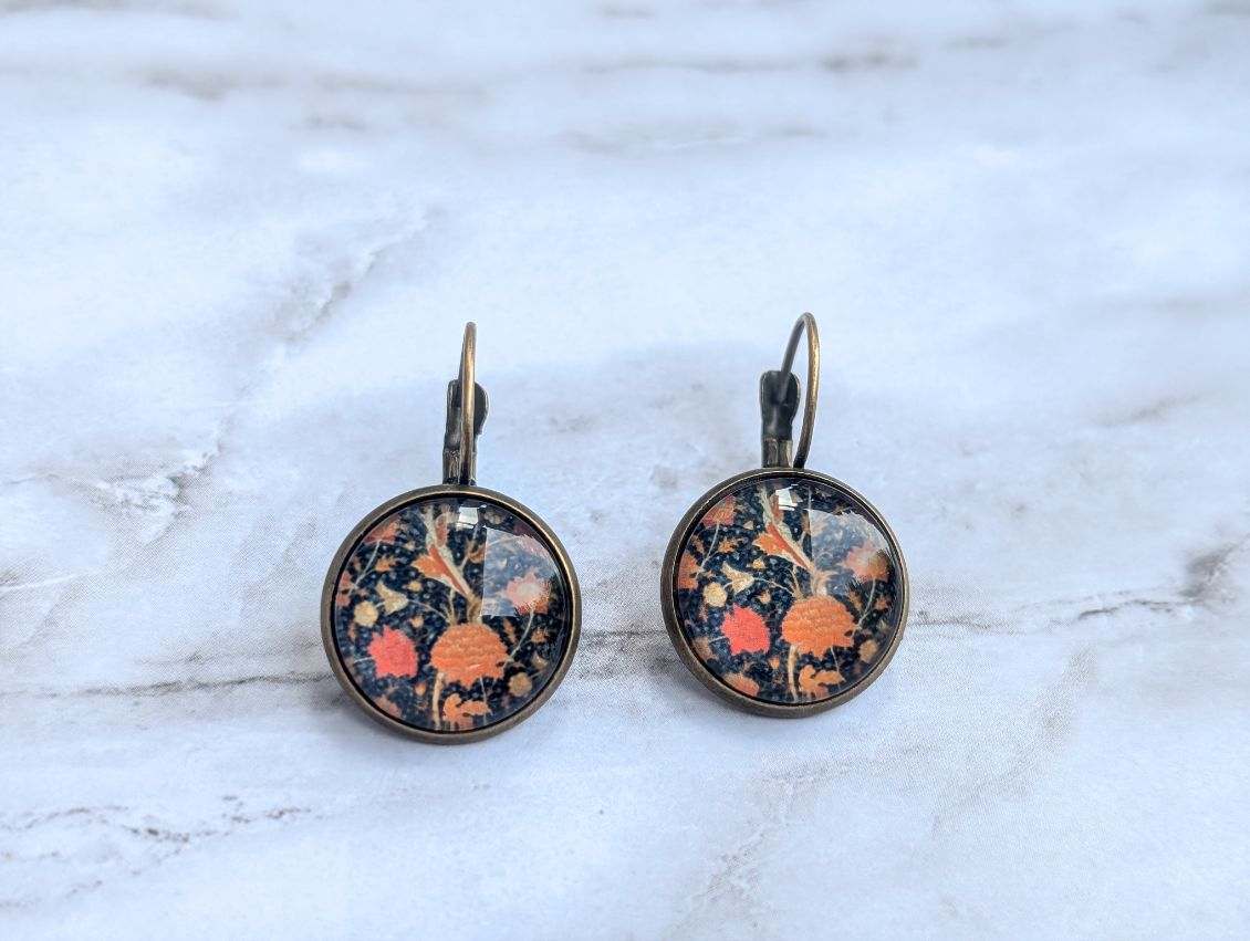 Round floral leverback earrings with orange and blue botanical print on dark background.