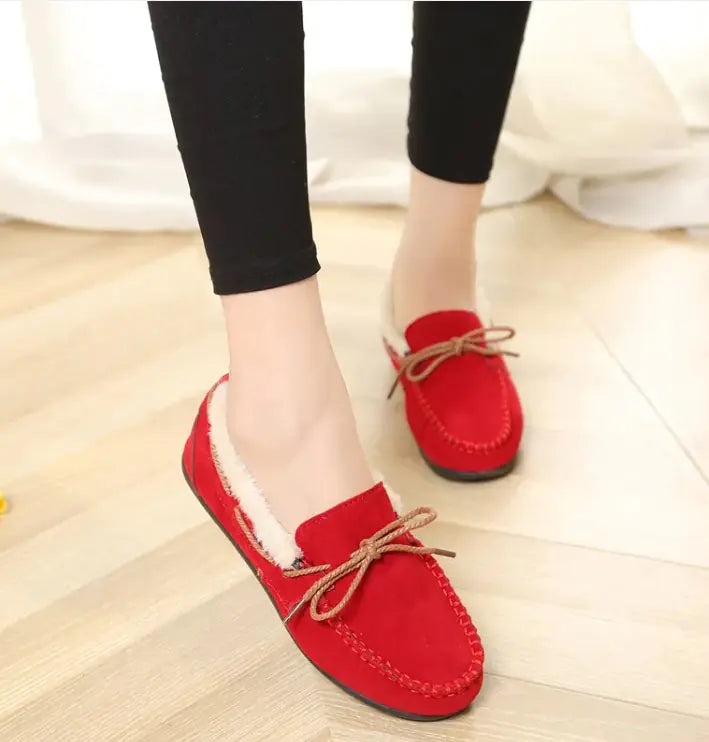 Red plush slip-on moccasin flats with lace-up bow and fuzzy lining, worn