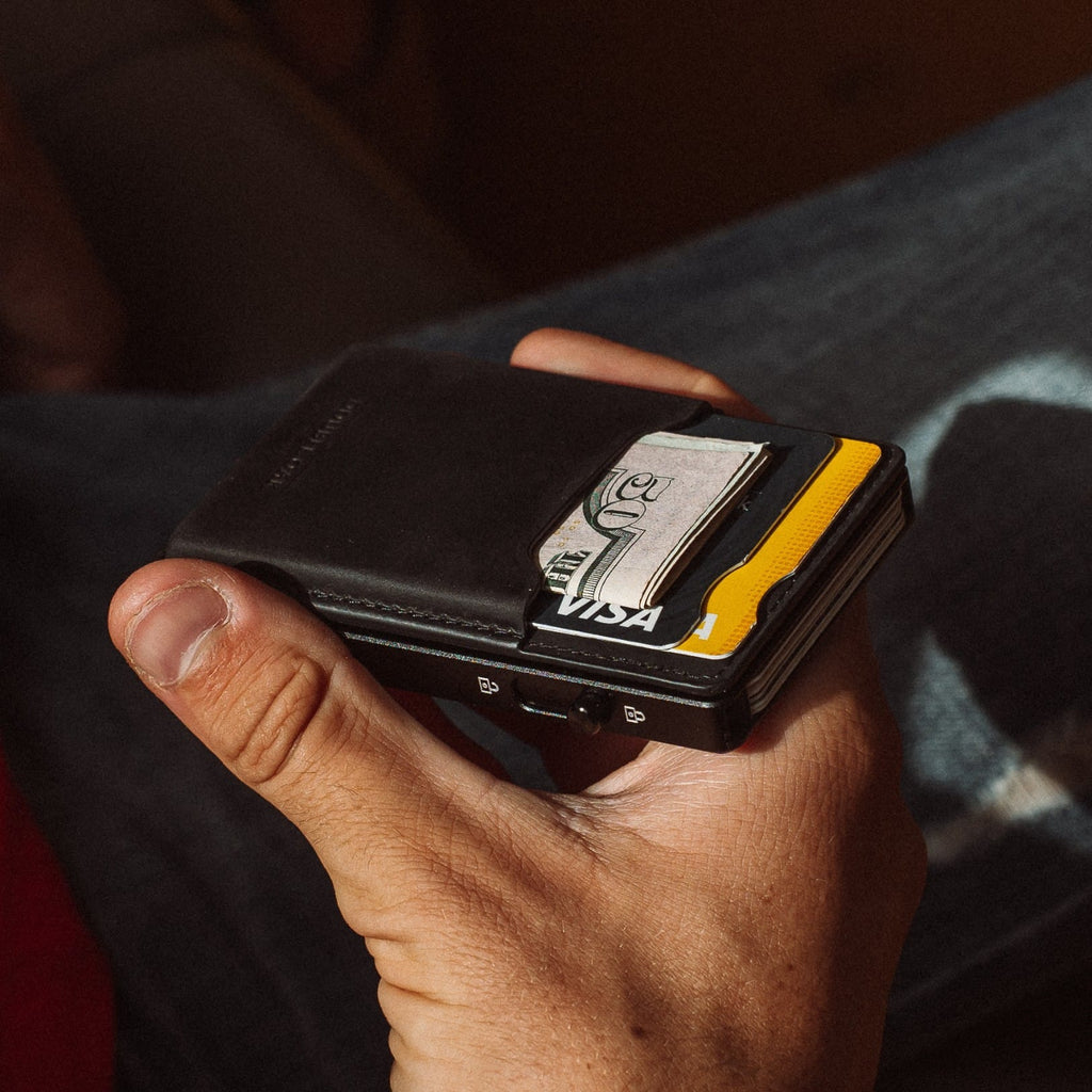 Black leather cardholder wallet with card slots and yellow accents, held by fingers.