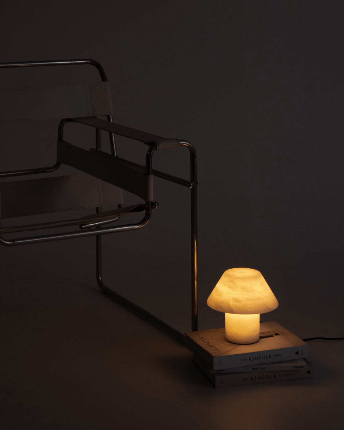 Small lit table lamp with fabric cone shade and cylindrical base on stacked books