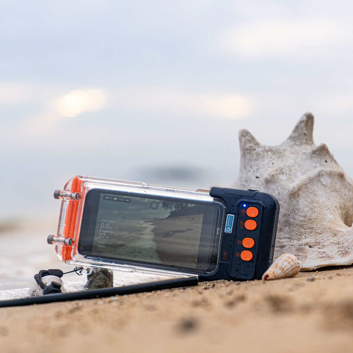 Waterproof phone case on sand with clear front window and orange button controls.