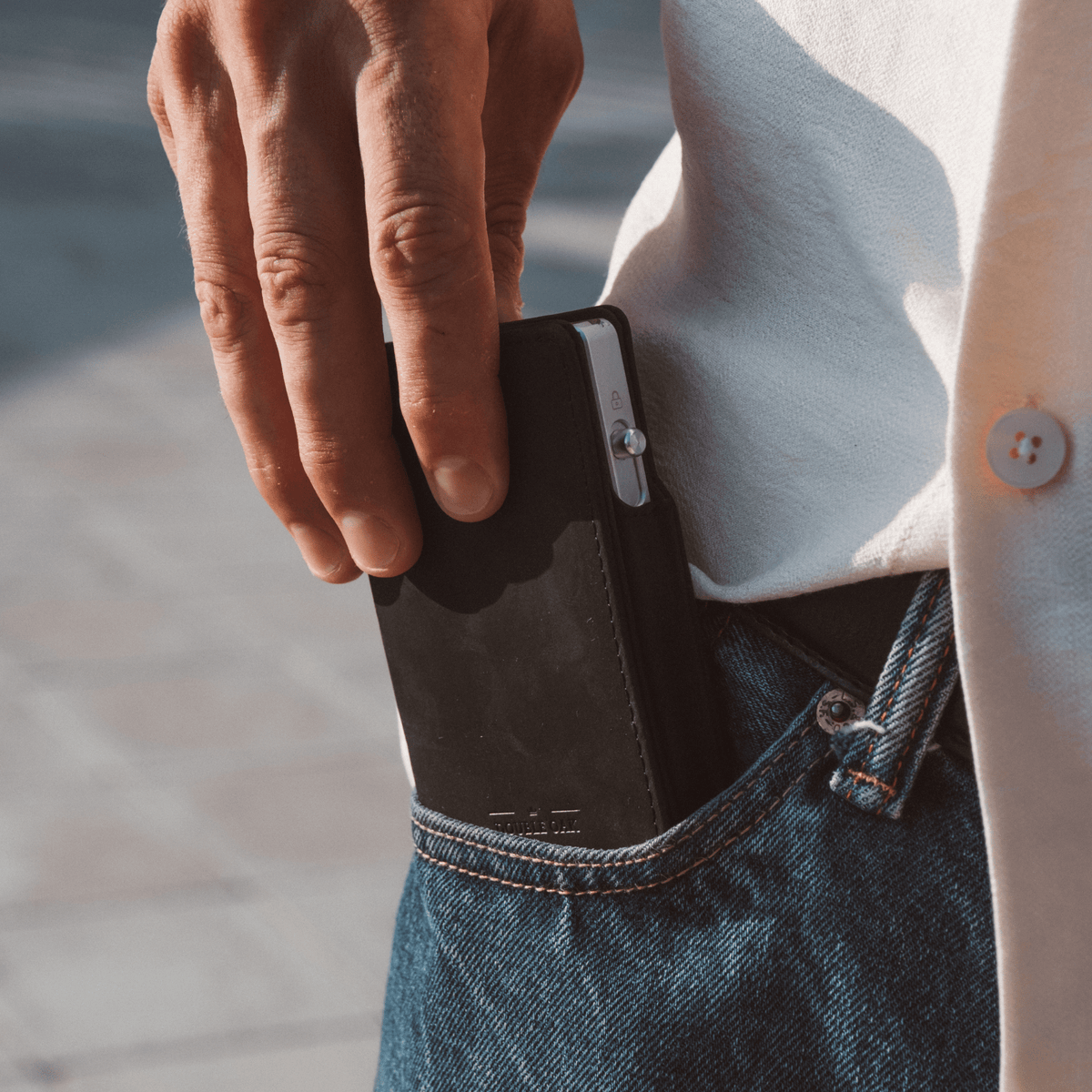 Dark bifold wallet with card slot visible, held beside denim jeans pocket