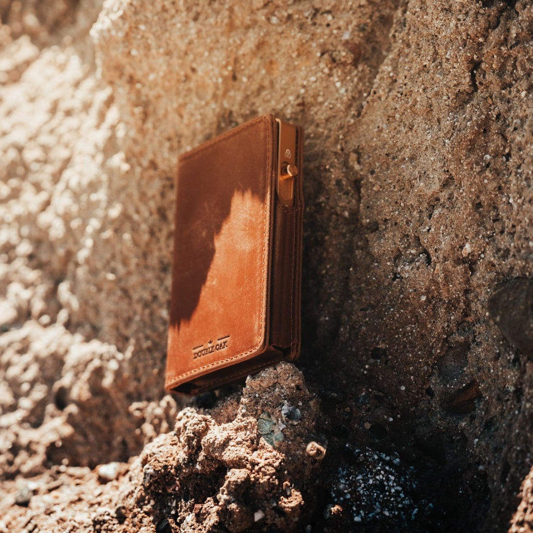 Brown bifold wallet with card pocket and small metal loop, outdoors on rock surface