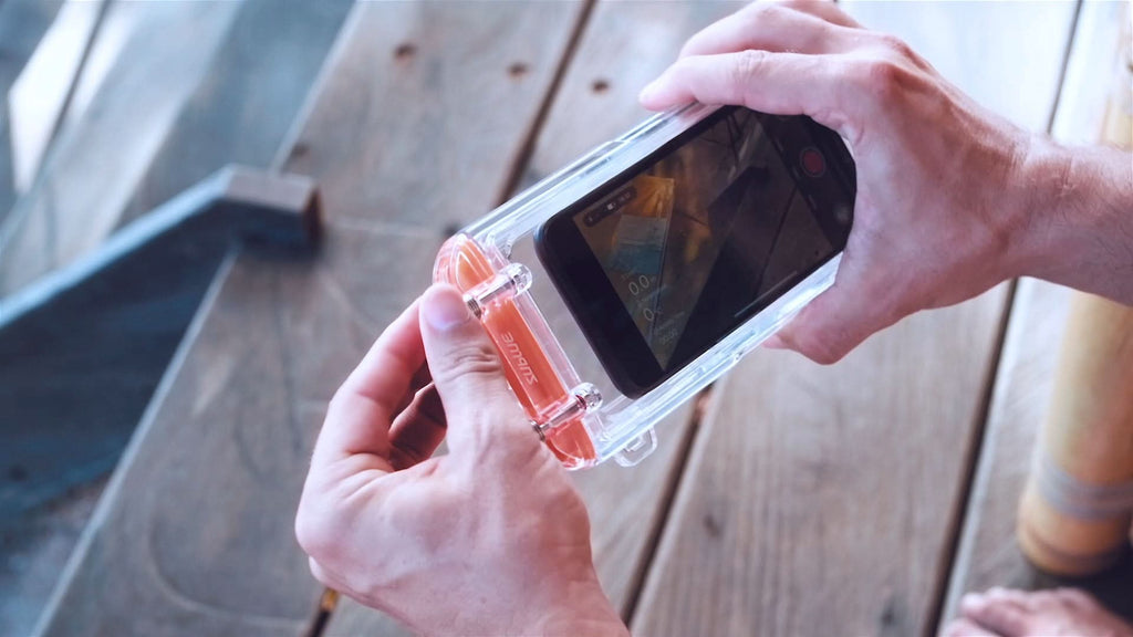 Hands holding a clear waterproof phone case with orange-tinted latch and front window.
