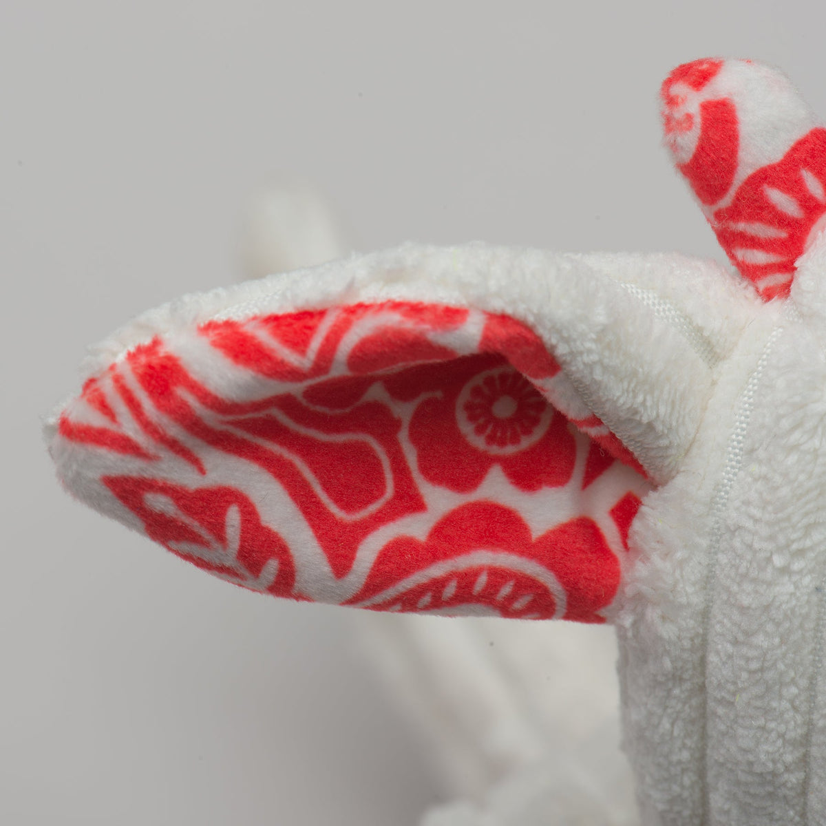 Close-up plush dog toy ear with red-and-white patterned fabric and white textured fur