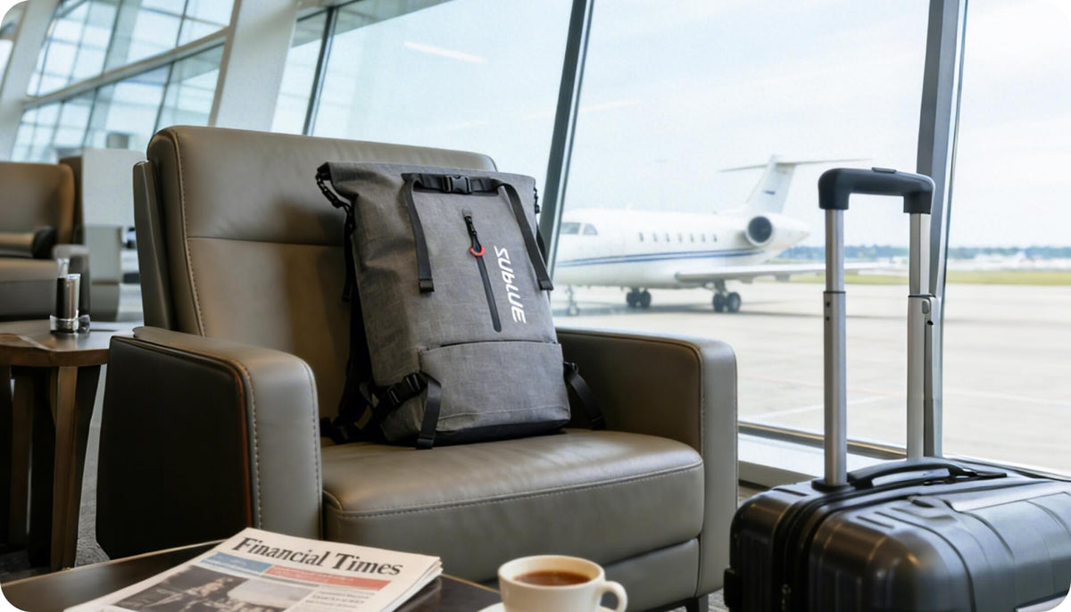 Gray waterproof 30L roll-top backpack on a lounge seat beside a carry-on suitcase