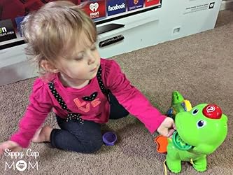 Small child playing with green counting dinosaur toy with number buttons on belly