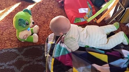 Green plush song-learning bear toy and a baby playing on a blanket
