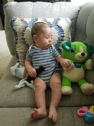 Green plush song-learning bear toy beside a baby on a couch