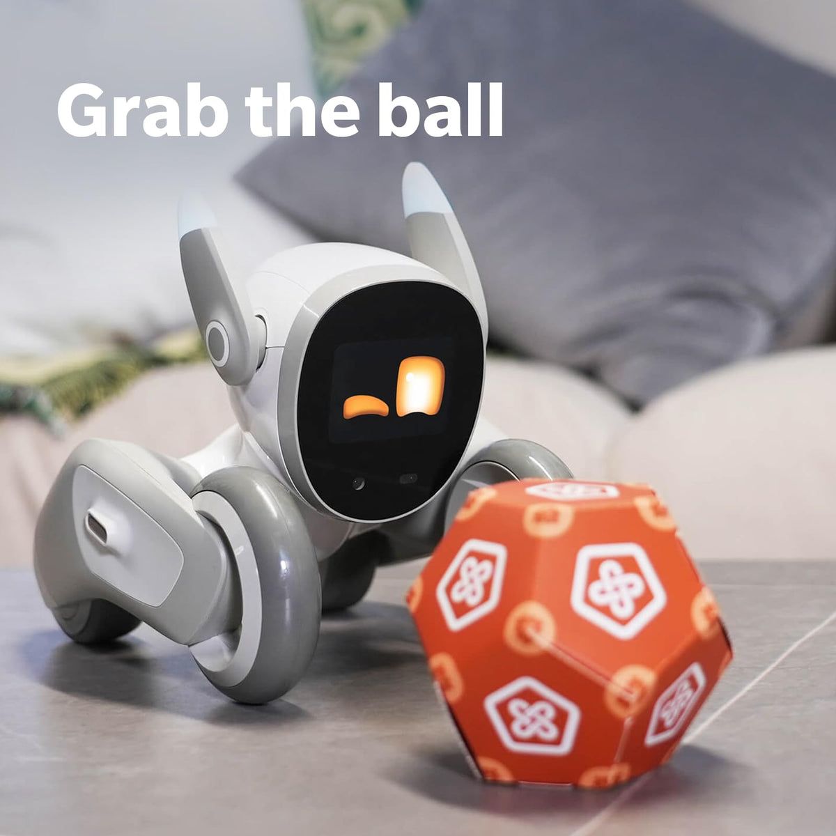White robotic dog reaching toward an orange ball on a couch