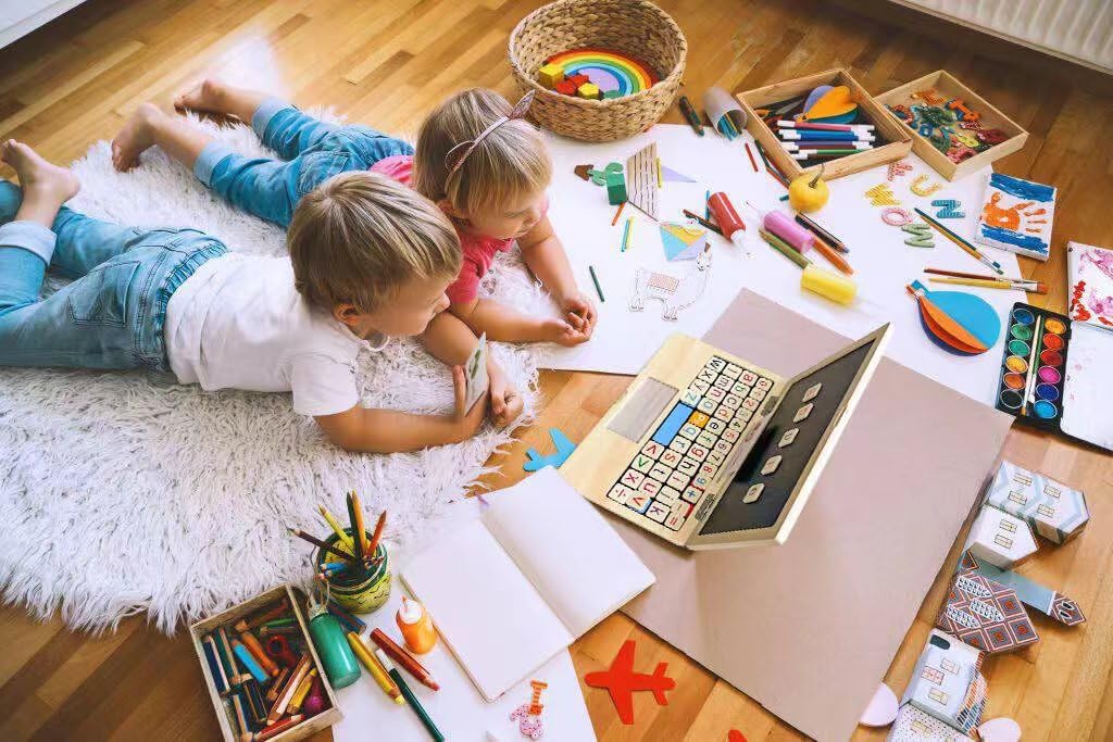 Toddlers playing with wooden learning laptop and magnetic tiles on the floor