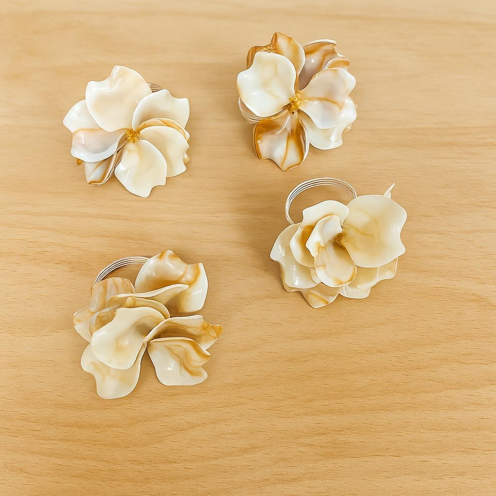 Four cream floral napkin rings with silver loops laid on a wooden surface