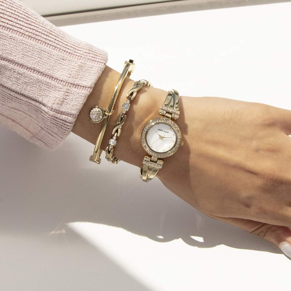 Gold-tone crystal-accented bangle watch and matching bracelet cuffs on wrist