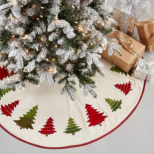 Round Christmas tree skirt, white with red border and multicolored embroidered trees, on floor