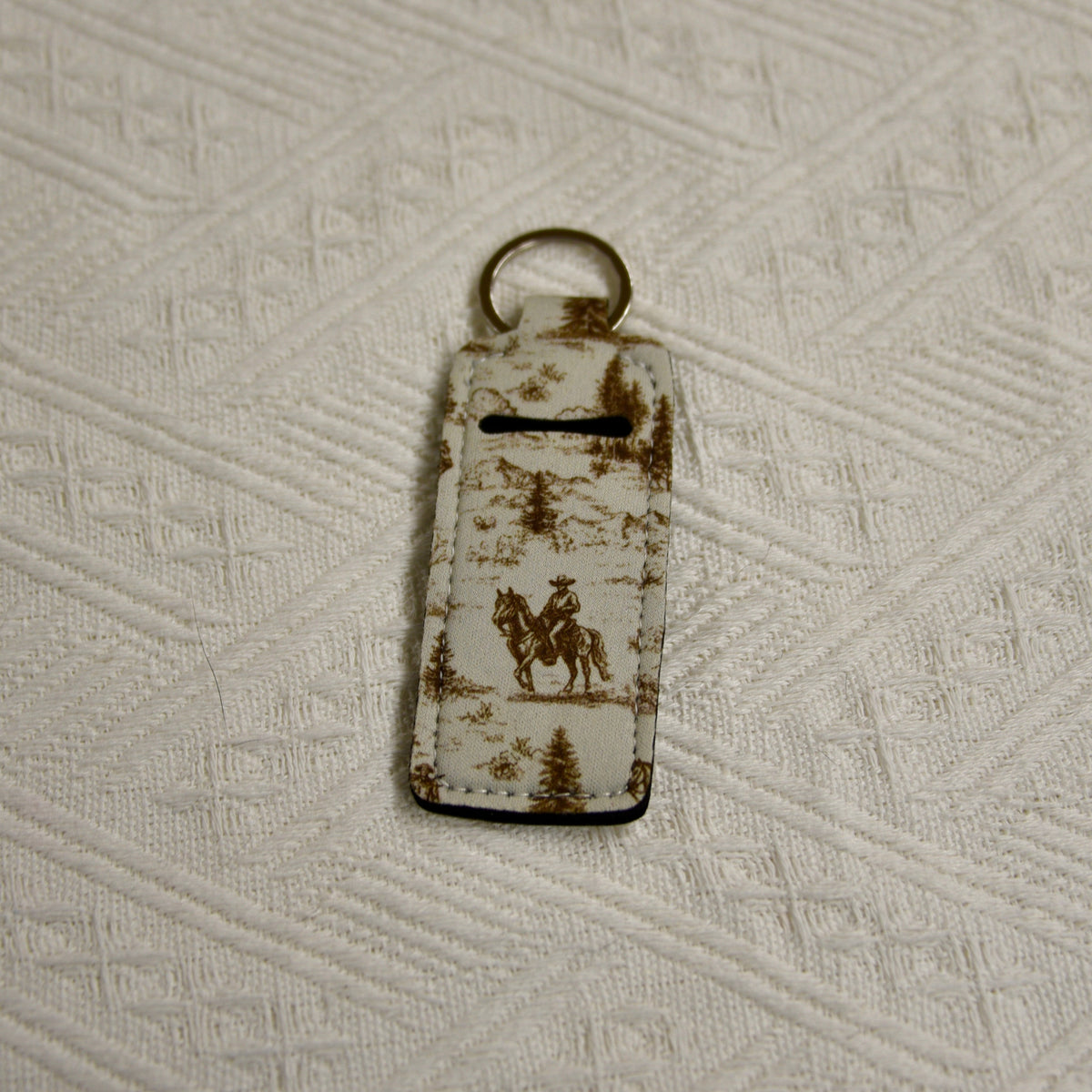 Tan Western chapstick holder keychain with cowboy and trees graphic, gold-tone ring