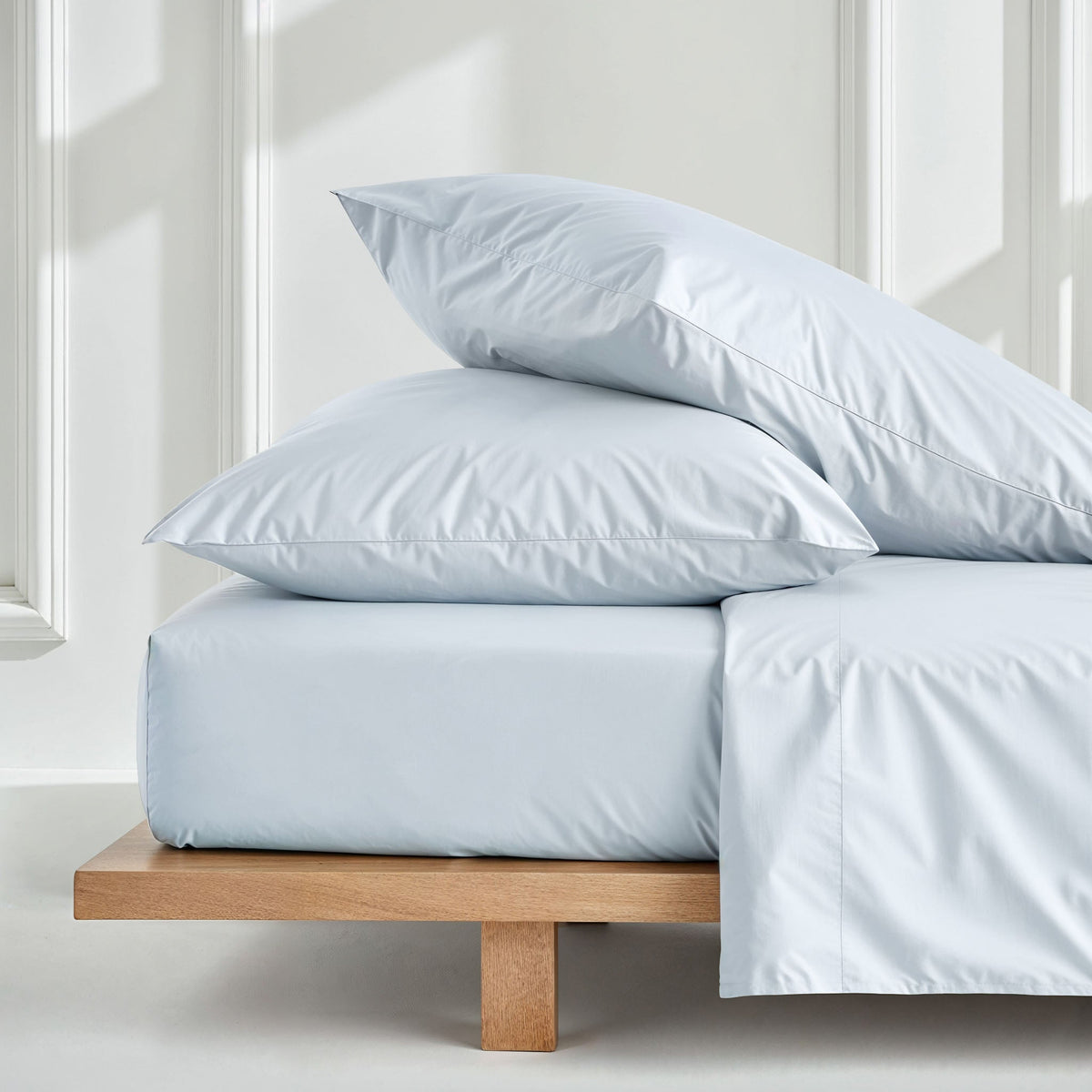 Australian sateen sheet set in light blue on a bed with stacked pillowcases
