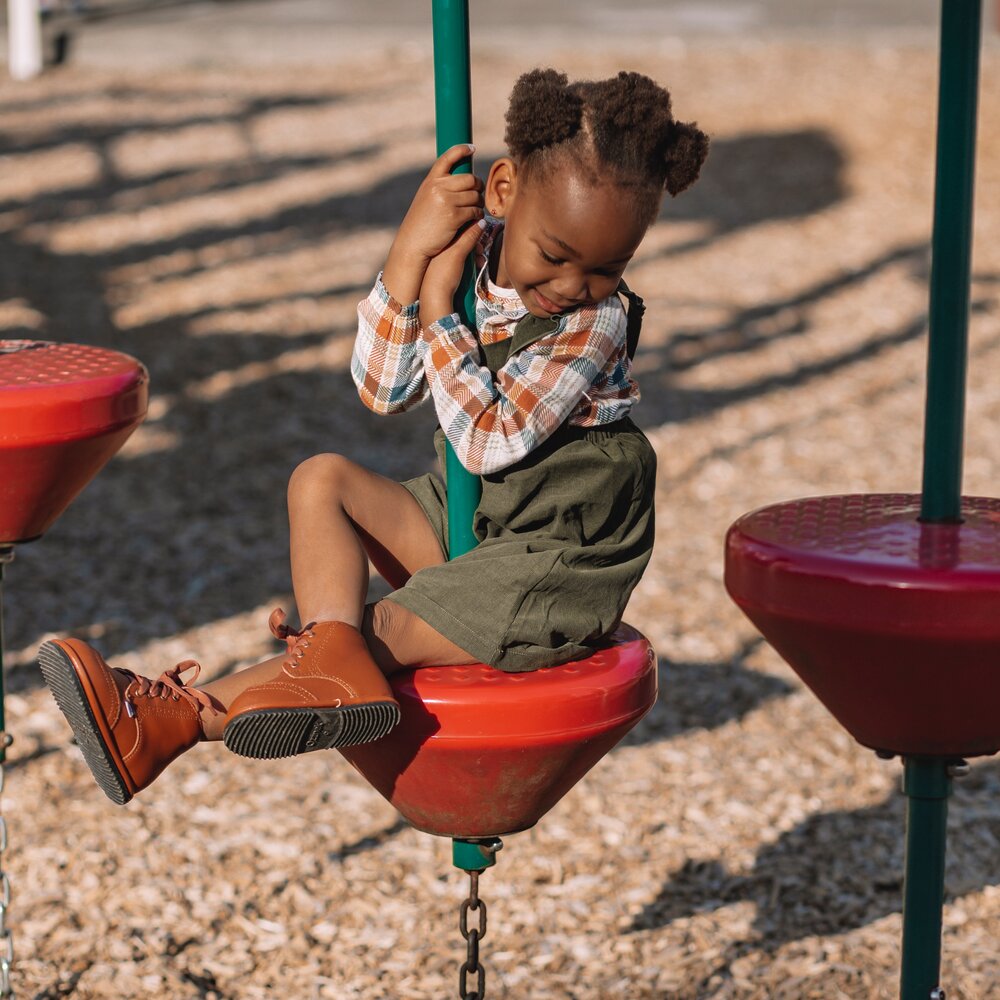 Brown toddler lace-up shoes with rubber sole, worn outdoors at playground