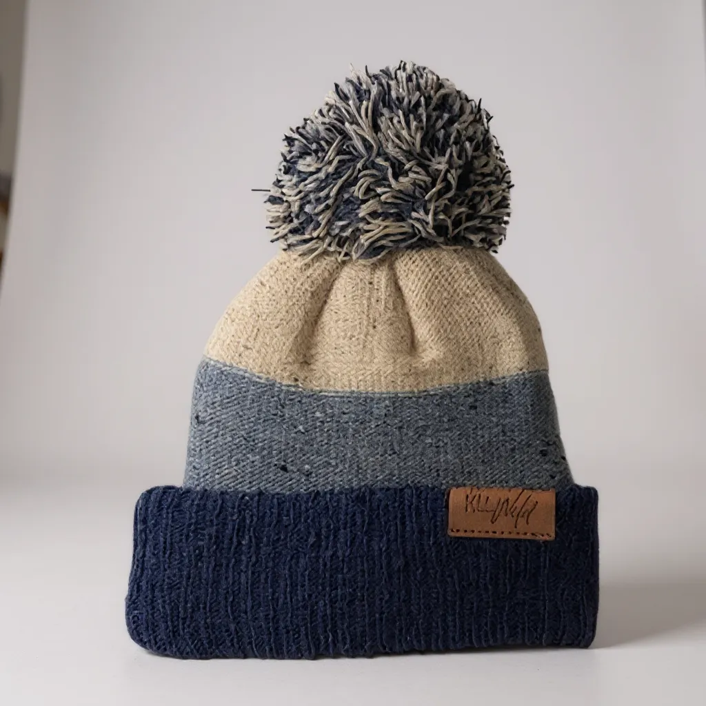 Puff-knit beanie in navy with gray pom-pom, cream crown, and tan leather brand patch