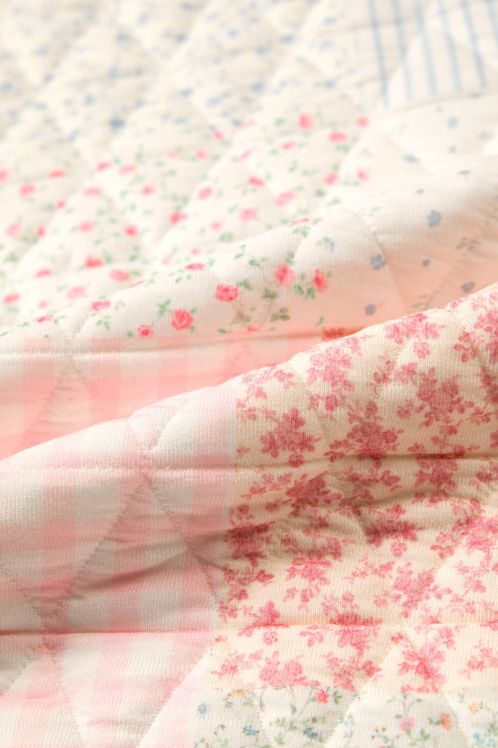 Quilted patchwork fabric close-up, pink floral blocks and light blue grid