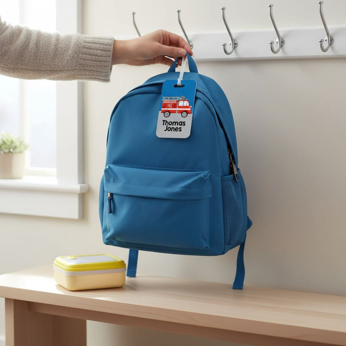Blue fire truck backpack with attached rectangular name tag reading 'Thomas Jones'
