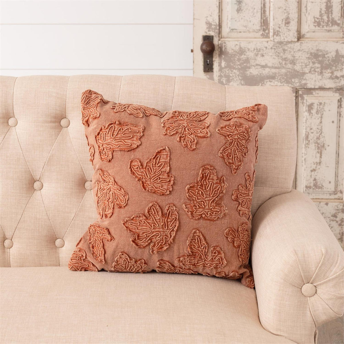 Orange stonewashed throw pillow with raised leaf embroidery, angled front view, square