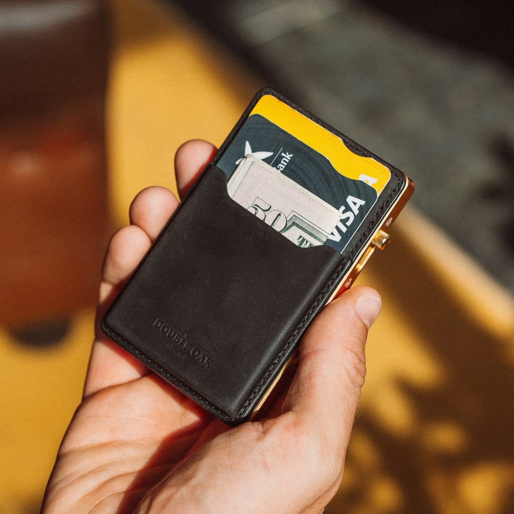 Black leather cardholder wallet with cards and yellow trim, held in hand.