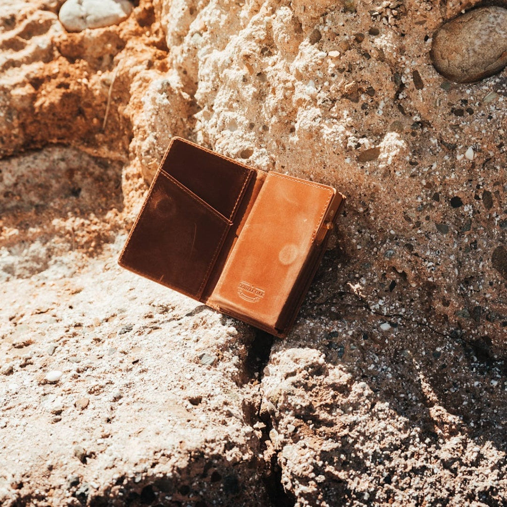 Brown bifold leather wallet with card slots, shown outdoors on textured ground