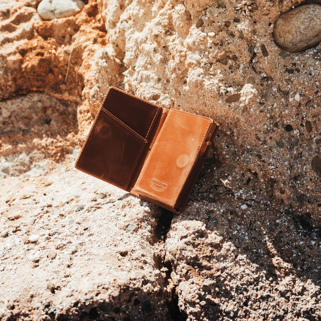 Brown bifold leather wallet with card slots, shown outdoors on textured ground