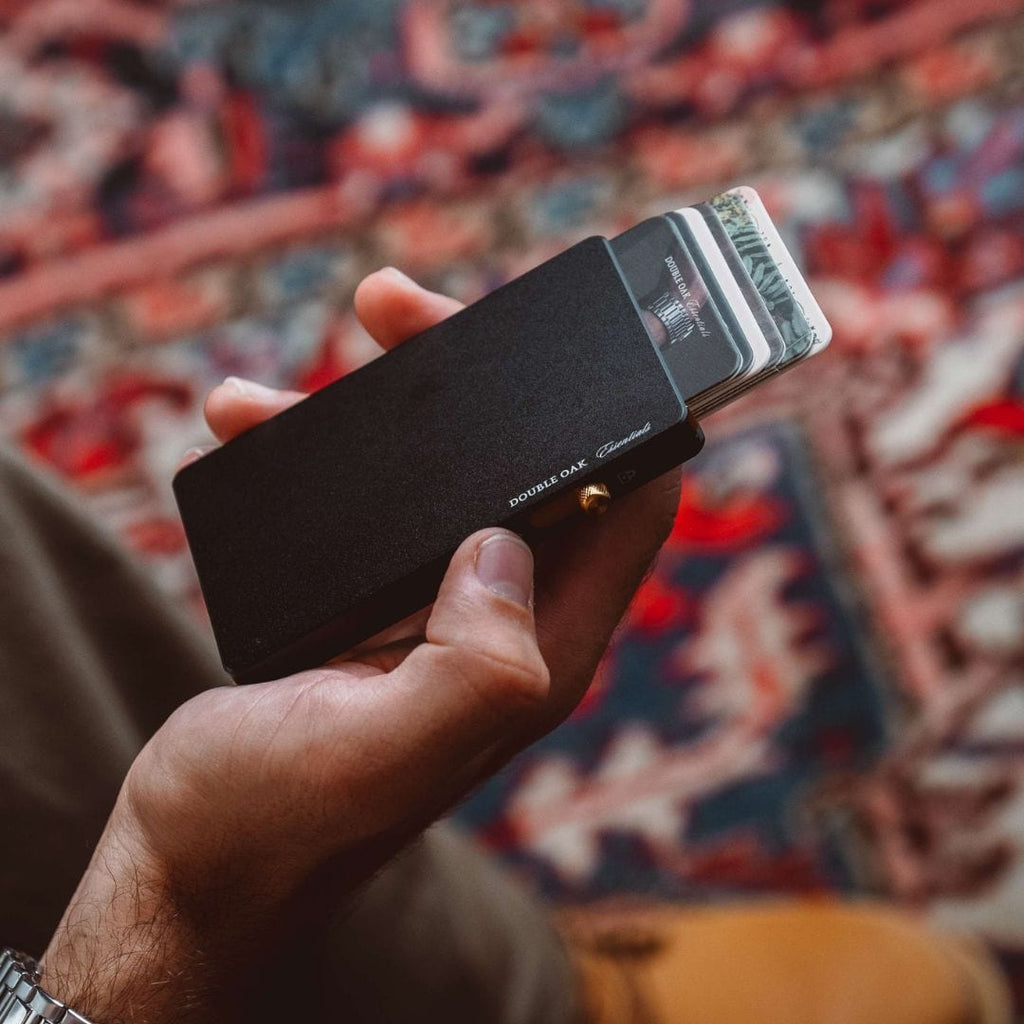 Matte black pop-up cardholder with bills tucked inside and brass button closure.