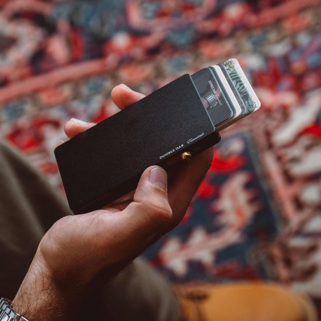 Matte black pop-up cardholder with bills tucked inside and brass button closure.