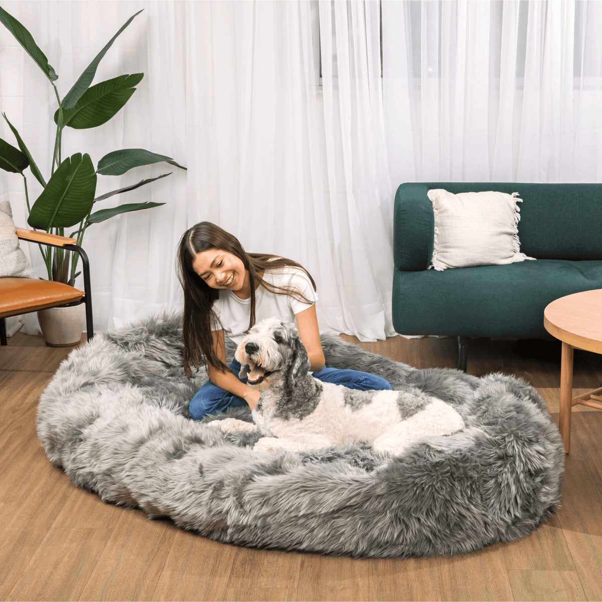 Charcoal grey round faux fur dog bed with a person and a dog sitting comfortably
