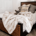 White faux-fur waterproof throw blanket draped over a couch with brown-trim accents