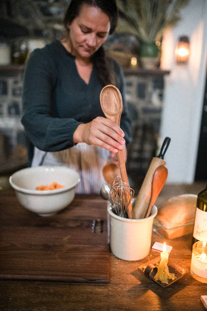 Wooden spoon held above a bowl of food, showing an oval bowl and long handle.