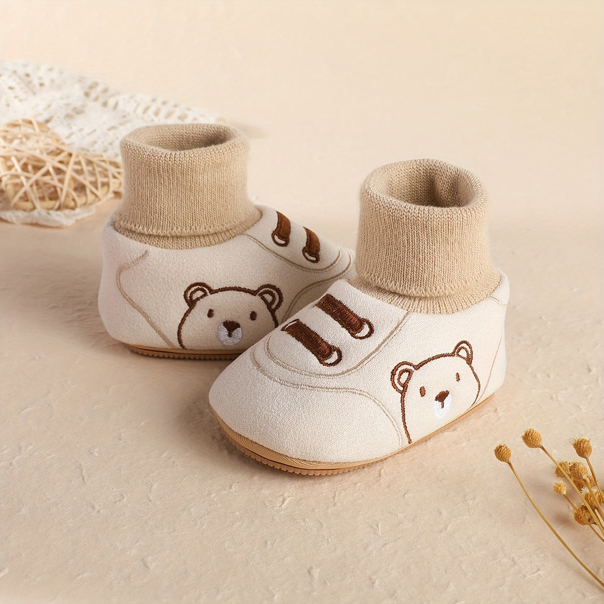 Pair of cream baby sock booties with bear face and brown lace-like stripes