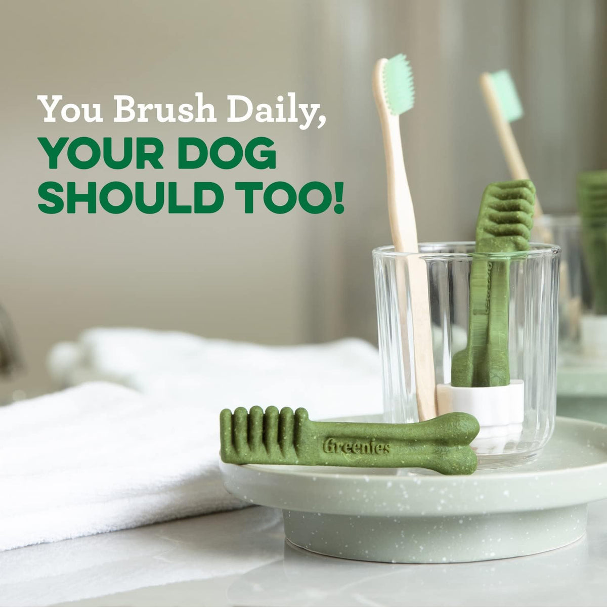 Greenies green dental chew resting on a bathroom sink near a toothbrush cup