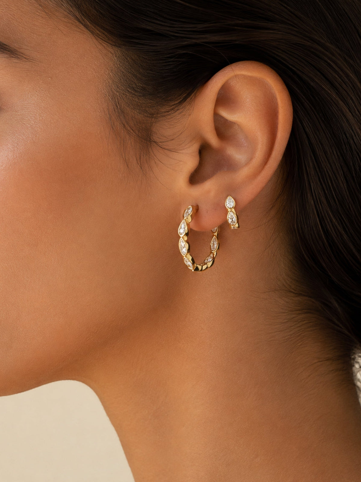 Small gold hoop earrings with marquise-cut crystal stones, worn on the ear