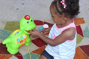 Child using green counting dinosaur toy with open mouth and colorful number panel
