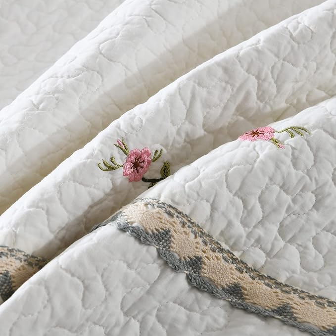 White quilt with quilted texture and pink floral embroidery on decorative edge strip