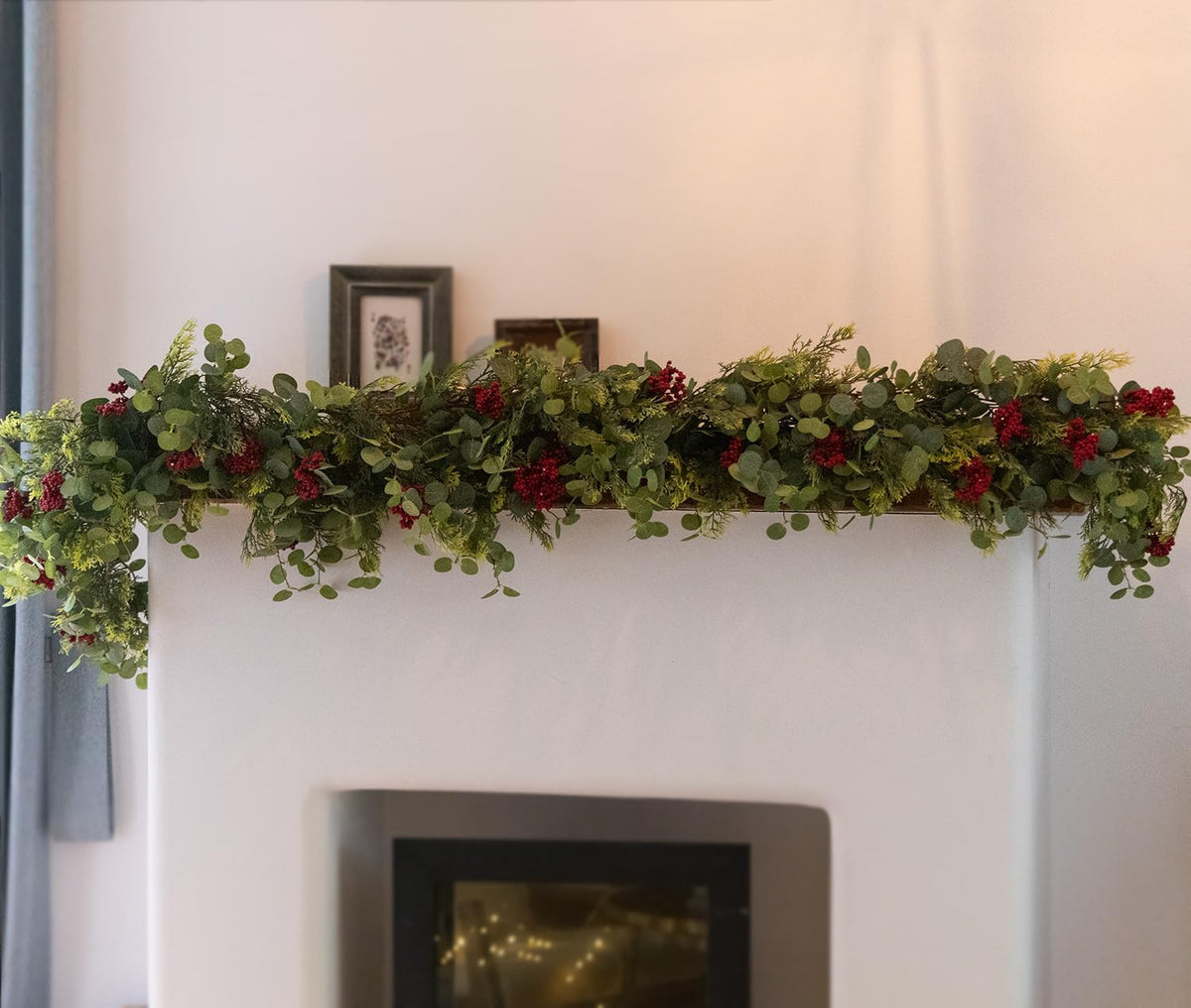 Long artificial greenery garland with green leaves and red berry clusters across a wall