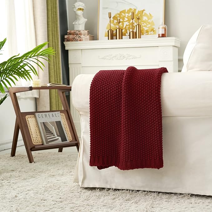 Wine red chunky cable-knit cotton throw blanket draped over a sofa arm.