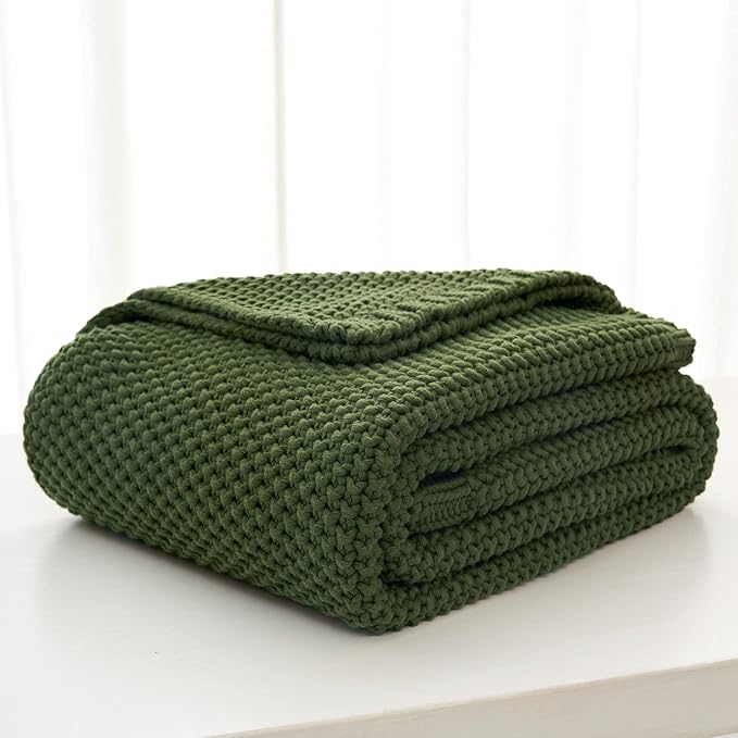Folded olive green chunky cable-knit throw blanket on a white surface