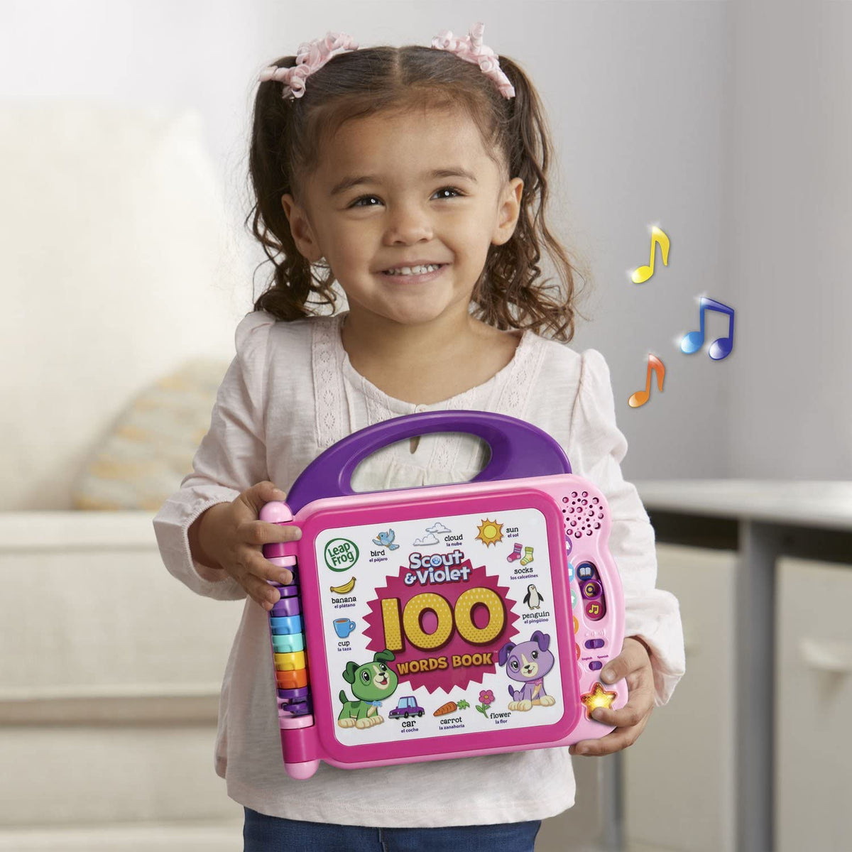 Smiling child holding purple and pink bilingual 100 words book toy with side speaker lights