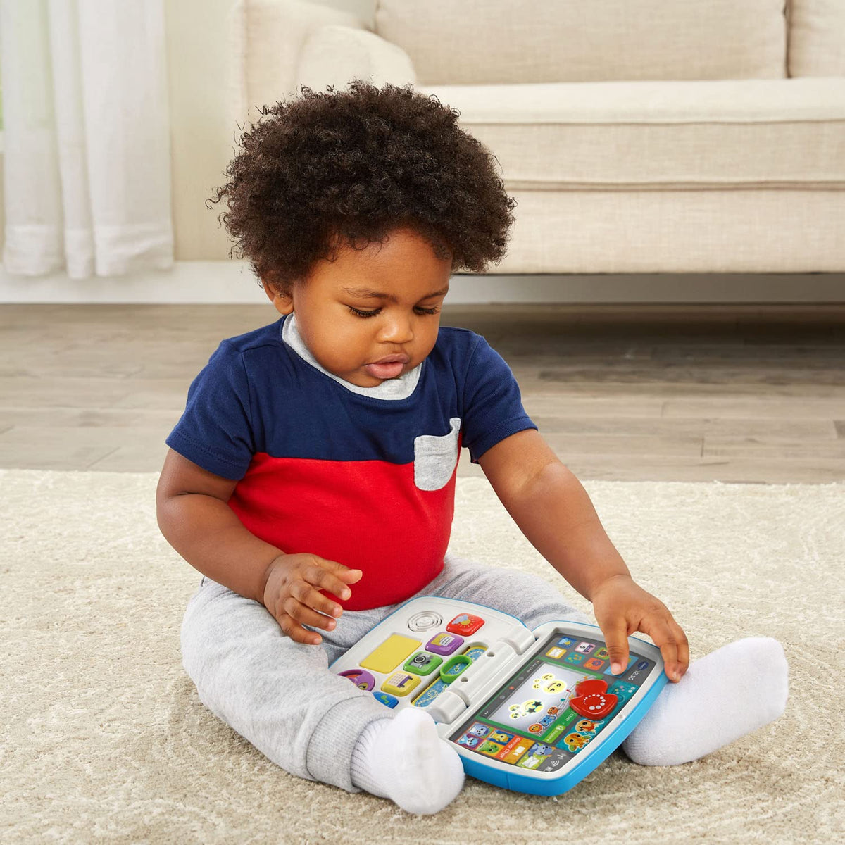Toddler using a blue interactive laptop toy with colorful buttons on the tray