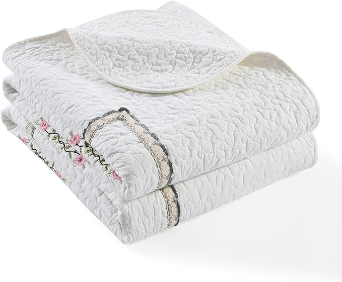 Folded white quilt coverlet with embroidered floral accent and light border trim