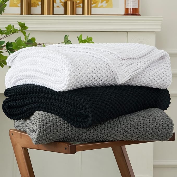 Stacked chunky cable knit throw blankets in white, black, and gray.