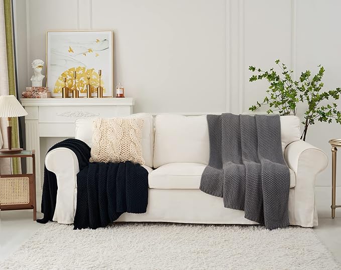 Chunky knit throw blanket in dark navy draped over a sofa with a cream throw nearby.