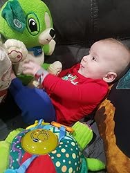 Baby playing with green plush song-learning bear on a living room couch