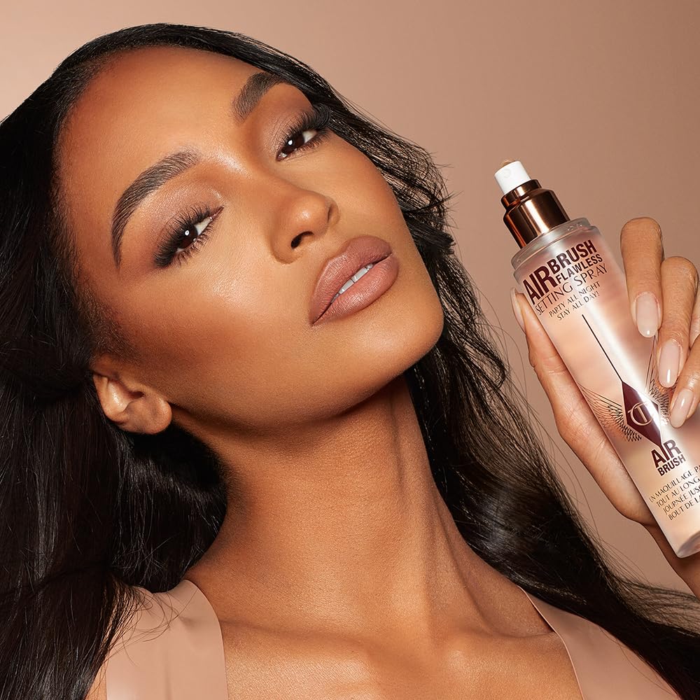 Model holding Charlotte Tilbury Airbrush Flawless setting spray bottle near cheek
