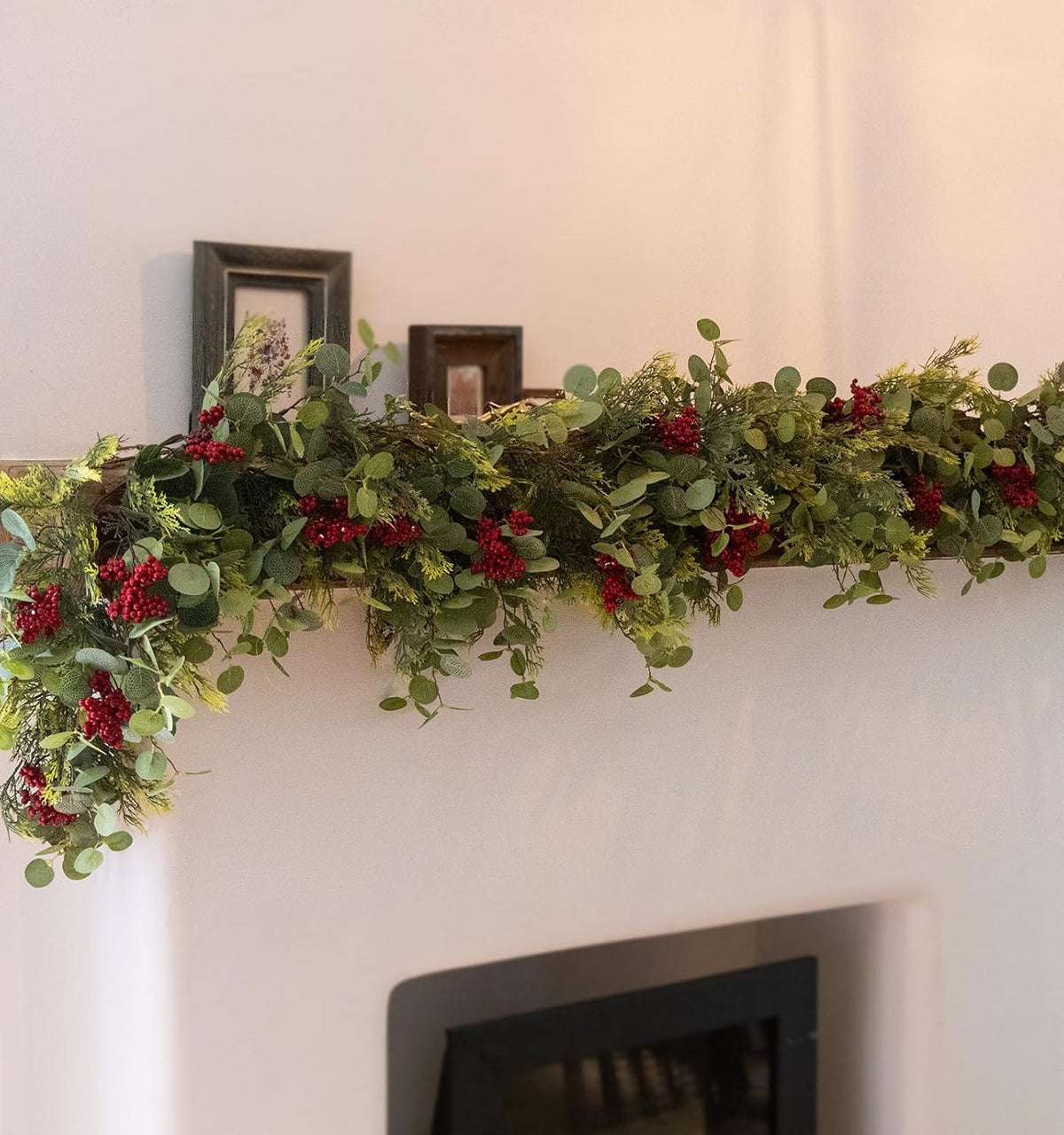 Artificial holiday greenery garland with eucalyptus leaves and small red berry clusters above fireplace