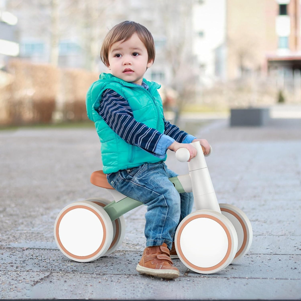 Toddler riding balance bike on pavement with green frame, orange seat, and white wheels